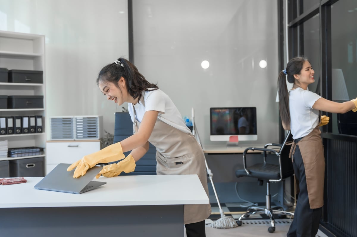 Two housekeepers working together to clean windows and floors in a living space