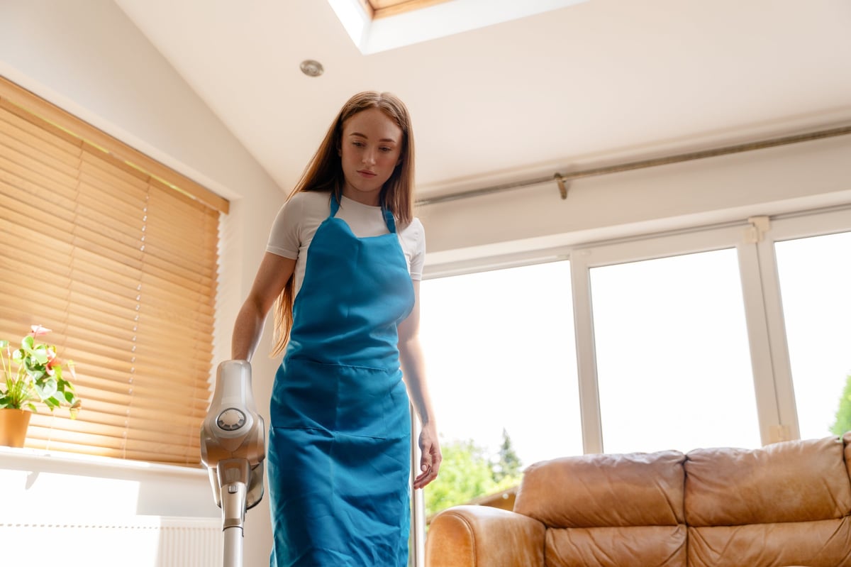 Cleaner vacuuming a bright living room as sunlight streams through the windows